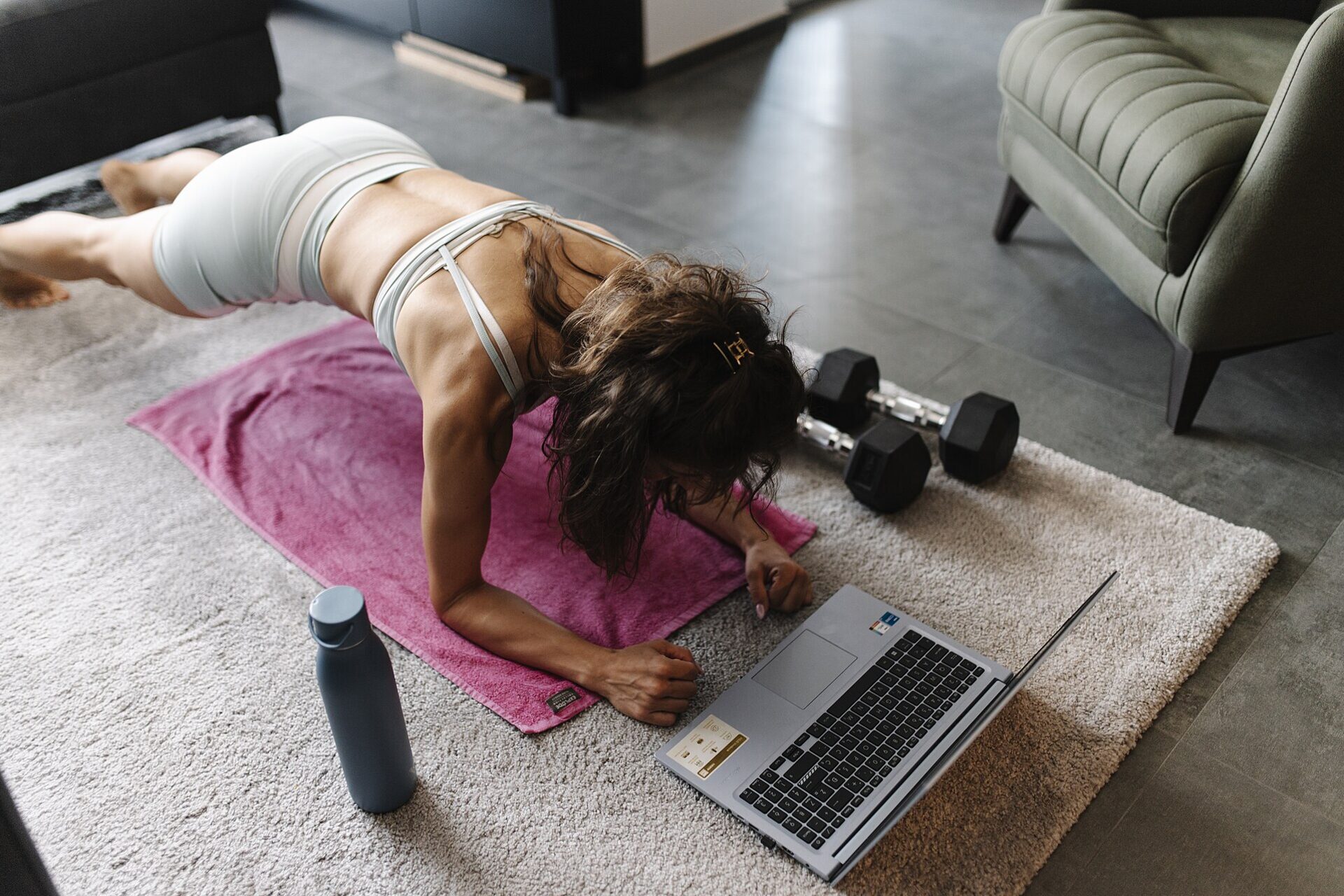 A woman working through a floor exercise at home while following a session on a laptop.