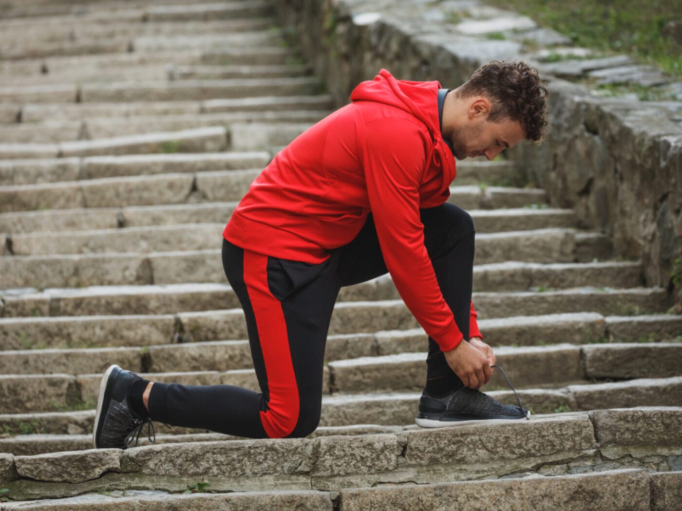 A runner in a red top stretching on a flight of stone steps.